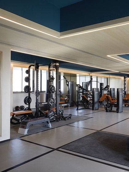 The gym at 'The Bandra Project' features state-of-the-art equipment and a clean, modern design. Mirrored walls enhance the sense of space, while the blue ceiling adds a pop of color.