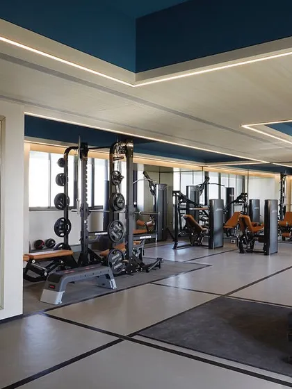 The gym follows a grey, white, and black color palette, with blue painted ceiling coves and linear lighting to create a dynamic and motivating workout environment.