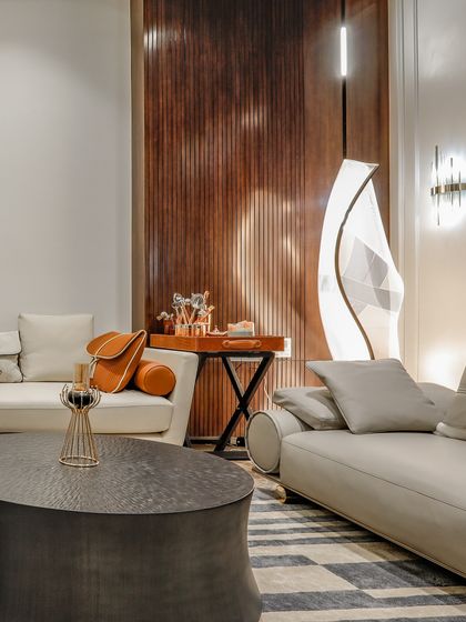 A detail shot of the living room furniture, featuring a sculptural floor lamp and a mix of sofa styles. The fluted wood paneling in the background adds another layer of texture.