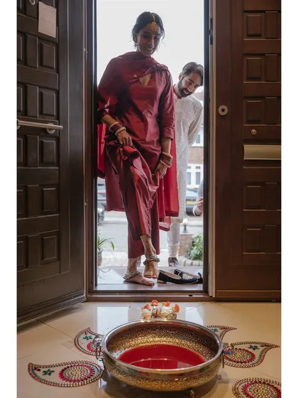 Shaan takes her first steps into her new home, a significant moment in the Griha Pravesh ceremony. The bowl of colored water and the rangoli mark the start of her new journey with Shubham's family.