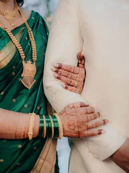 A detail shot focusing on the bride's hands, adorned with henna and green bangles, holding the groom's arm. This image highlights the beautiful traditions and symbolism of a Maharashtrian engagement.
