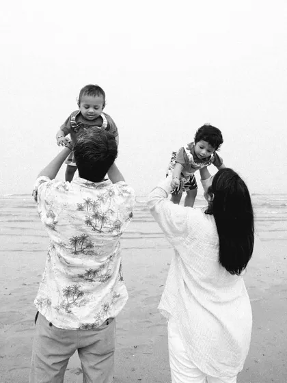 A beautiful black and white photo of parents lifting their twin babies up at the beach, creating a timeless family memory.