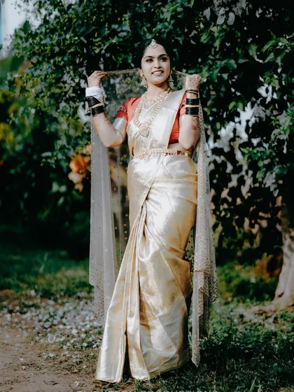 A beautiful solo portrait of a bride in a classic off-white and red silk saree, a staple of many South Indian weddings.