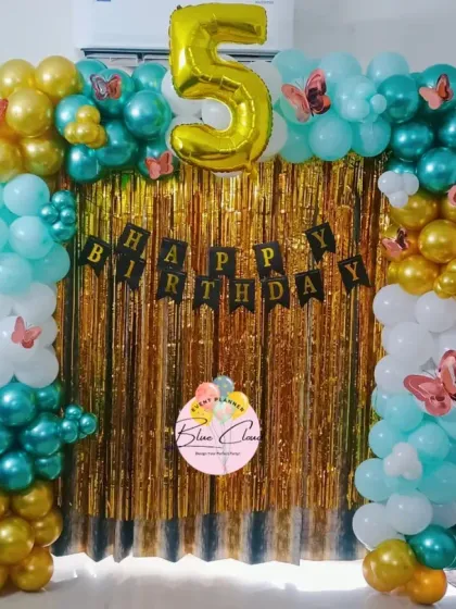 A teal and gold butterfly-themed balloon arch with a gold shimmer curtain for a 5th birthday.