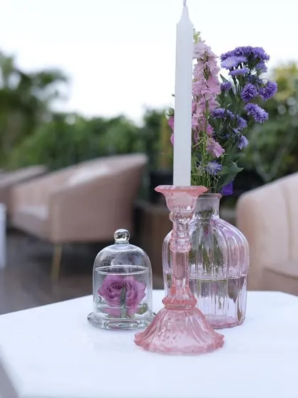 A close-up of a centerpiece from Reeya and Parth's wedding, featuring a single rose under a glass cloche and a pink candle holder.