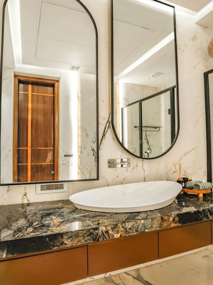 This guest bathroom features a dark marble countertop with a unique vessel sink. The dual arched mirrors with black frames add a modern, graphic element to the space.