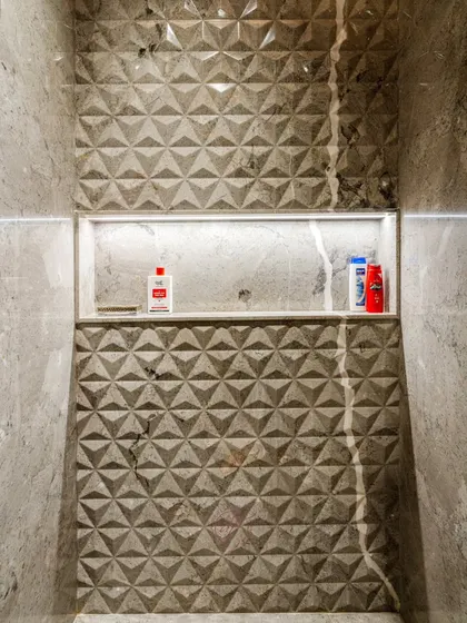 The recessed shower niche with integrated lighting is a practical and modern storage solution. The 3D geometric tiles create a beautiful, textured backdrop.