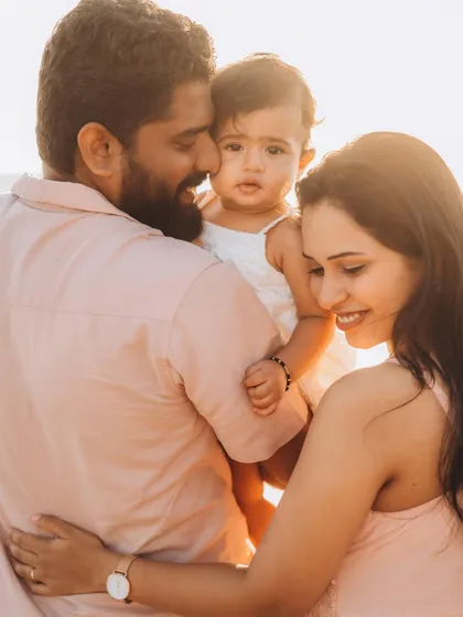 A close, sun-kissed portrait of a young family. The father holds their baby close as the mother leans in, their expressions full of warmth and affection. This is the essence of a lifestyle family photoshoot, capturing love in its purest form.