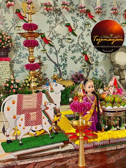 A close-up of a baby shower decoration, showing the beautiful blend of a Pichwai-style backdrop, traditional dolls, and a cow-and-calf figurine, all symbolizing prosperity and care.