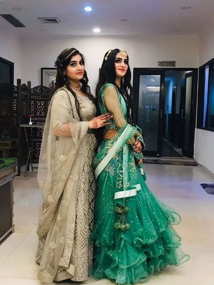 Two clients looking beautiful in their chosen outfits, one in a beige lehenga and the other in a sea-green ruffled lehenga.