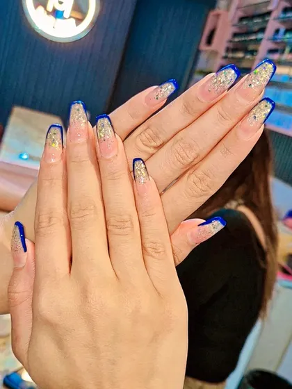 A glamorous take on the French manicure, featuring coffin-shaped nails with a deep blue tip and a cascade of gold glitter. This design is perfect for parties and festive events.