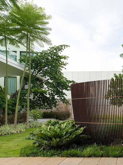 A curved Corten steel screen provides a sculptural boundary for a residential lawn. The design uses the screen to create privacy while adding an artistic element that complements the modern architecture and surrounding greenery.