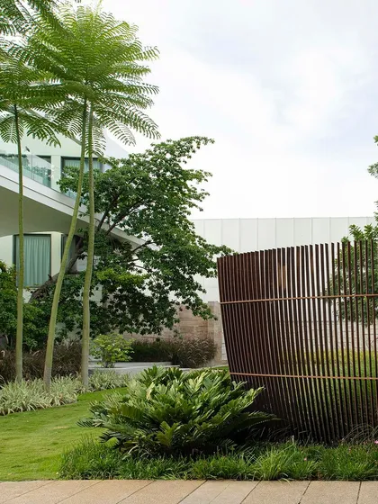 A curved Corten steel screen provides a sculptural boundary for a residential lawn. The design uses the screen to create privacy while adding an artistic element that complements the modern architecture and surrounding greenery.