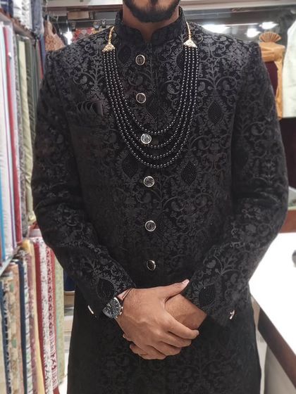 A close-up of a black self-jacquard sherwani, accessorized with a multi-layered black beaded necklace. This demonstrates how simple accessories can elevate a classic outfit.