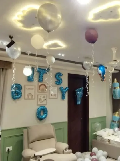 Room decoration for a newborn baby boy, with "IT'S A BOY" foil letters on the wall and helium balloons floating on the ceiling.