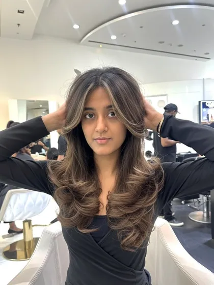 A beautiful color refresh with face-framing highlights. The lighter pieces around the face brighten the entire look, and the hair is styled in voluminous curls.