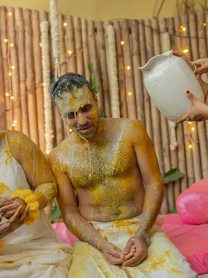 A family member pours water on the groom during the Haldi rituals, a moment of love and tradition.