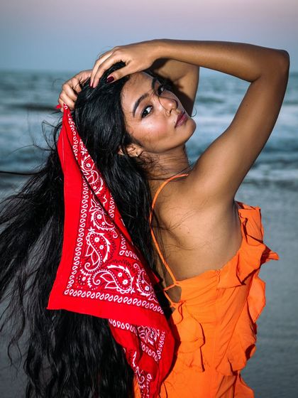This beach shot has a fun, retro vibe, using a bright red bandana as a key styling element. The ocean in the background and the wind in the model's hair create a dynamic, summery feel. The pose is confident and playful.