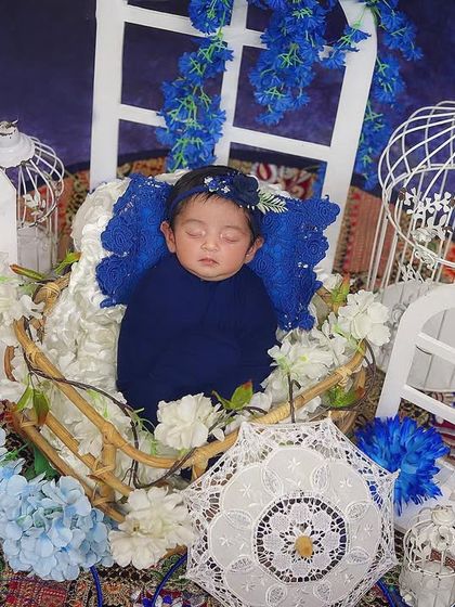 A beautiful portrait using shades of blue. This baby is surrounded by blue and white flowers, miniature windows, and birdcages, creating a whimsical and serene scene.