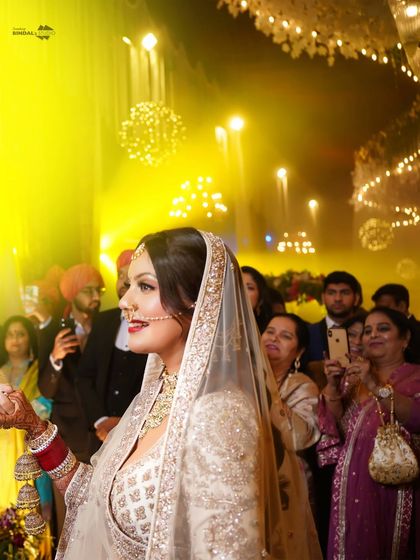 The bride's radiant smile as she walks down the aisle. The warm, yellow lighting and the guests in the background create a lively and happy atmosphere.