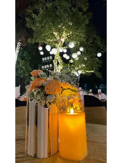 A simple yet elegant table centerpiece with a candle and flowers, set against the backdrop of trees wrapped in fairy lights. It's the small touches that create a magical ambiance.
