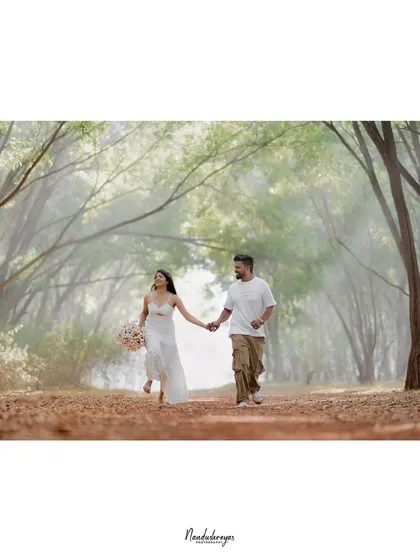 A wide shot of a couple holding hands and walking through a beautiful, misty archway of trees.