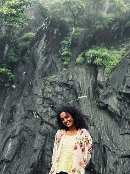 A happy trekker posing in front of a rocky cliff face.
