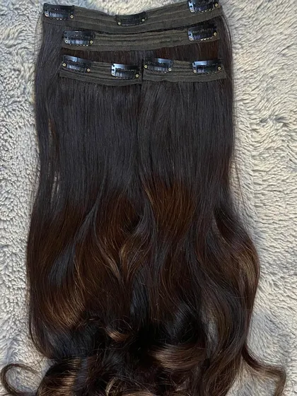 A look at a 4-piece clip-on extension set laid out. The dark hair with subtle highlights is designed to blend with natural hair while adding dimension and volume.