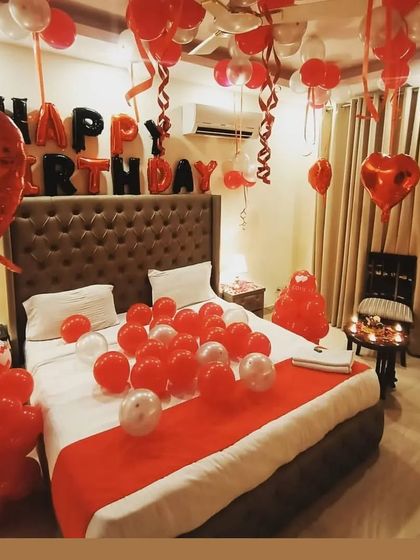 A full room decoration for a birthday, featuring a classic red and white theme. The setup includes 'Happy Birthday' foil balloons, balloons on the bed and ceiling, and balloon columns for a festive feel.