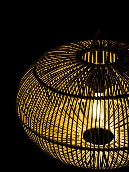 A detailed perspective of the flattened globe lamp, showing how the light source is nestled within the intricate web of woven rattan, creating a starburst effect.