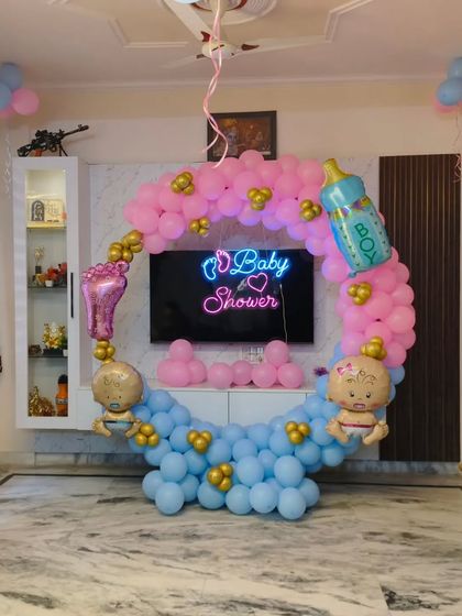 This baby shower decoration was designed to fit perfectly around the family's TV console. The pink and blue circular balloon arch with a neon sign creates a beautiful frame for the celebration.