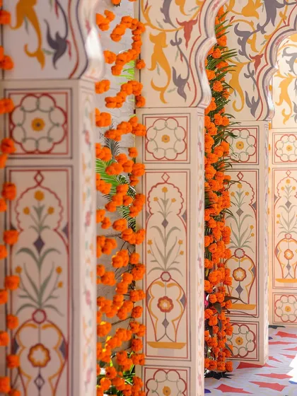A detailed view of the hand-painted motifs on the pillars of the entrance arches, accented with strings of fresh marigolds. This highlights the level of craftsmanship involved in creating the theme.