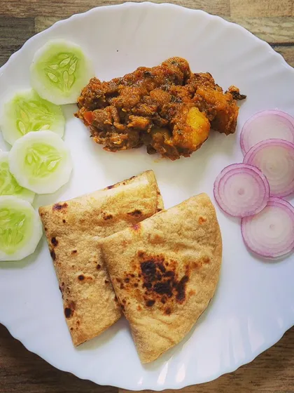 A simple, satisfying plate of desi khana. It features homemade roti with a dry Aloo Chicken curry, served with fresh cucumber and onion slices.