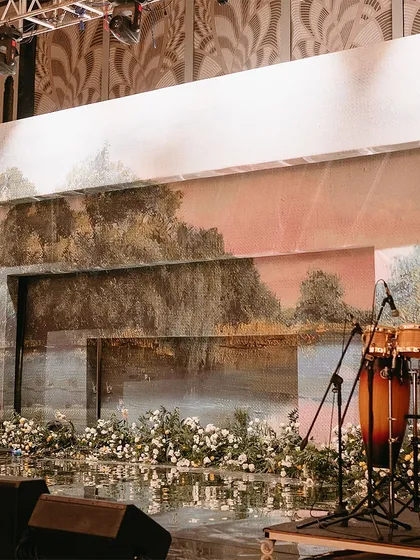 The stage backdrop for a Sangeet, featuring a painted canvas of a romantic landscape. This artistic touch, combined with a floor of white flowers, created a dreamy and elegant setting.