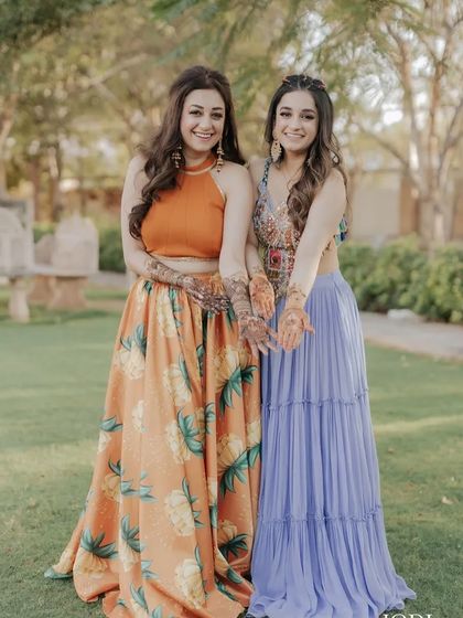 Two sisters showing off their Mehendi. Both have their hair styled in soft, open waves, a perfect choice for a relaxed and fun event.