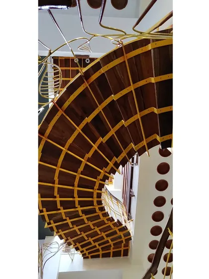 An upside-down view of a staircase reveals its intricate construction. The warm wood of the steps is complemented by the yellow-painted metal framework, showcasing how different composite materials can create a visually striking structure.