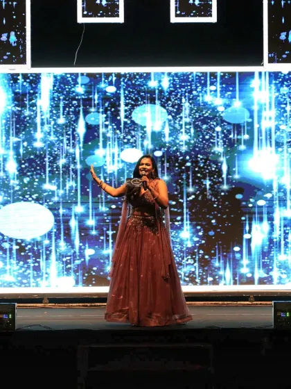 On stage during a Sangeet night, commanding the audience's attention against a stunning, glittering blue backdrop. This is where I feel most alive.
