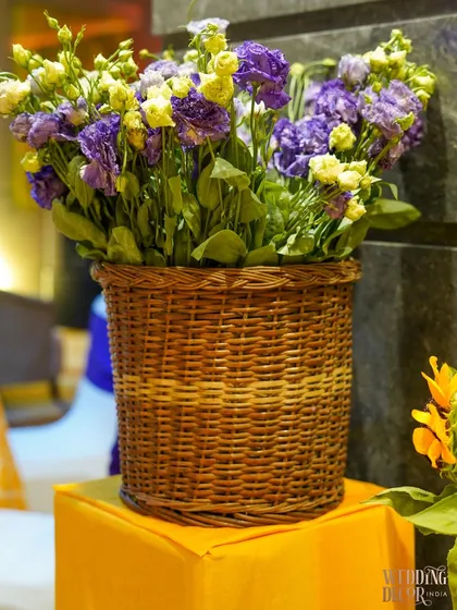 A wicker basket filled with a mix of yellow and purple flowers, demonstrating how we use complementary colors to create visually interesting arrangements.
