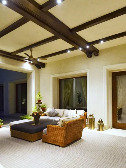 This project features intricate wooden ceiling designs that define this inviting living space. The outdoor sit out area is visible through the large doors, blurring the line between inside and out.