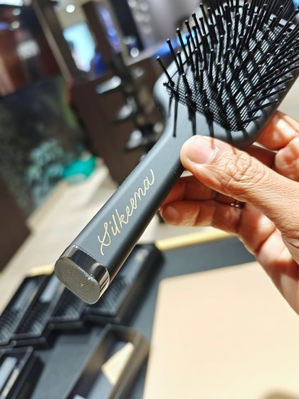A close-up of a personalized GHD hairbrush. The gold calligraphy on the matte black surface creates a beautiful, high-contrast look that feels very luxurious.