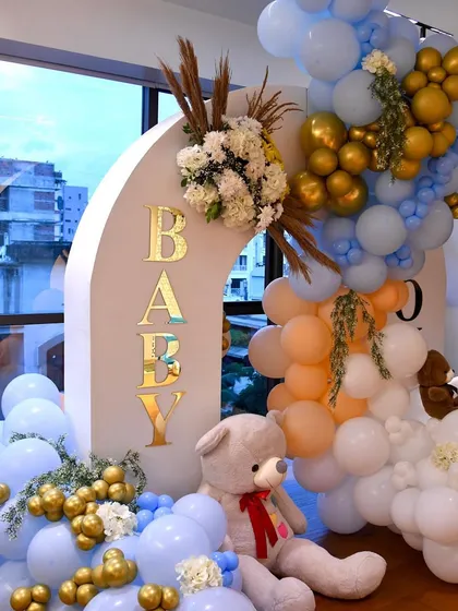 Welcoming a new baby with a grand balloon and floral installation. This double arch in pastel blue, peach, and gold is adorned with fresh flowers and a cute teddy bear.