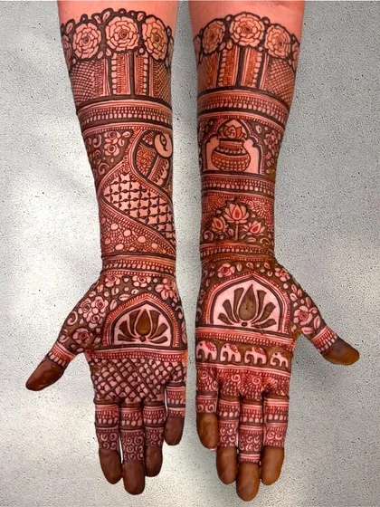 A traditional Indian mehendi design extending up the arms. It features classic motifs like the kalash, elephants, and lotus flowers, all tied together with intricate line and dot work.
