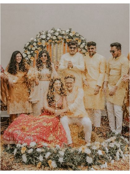A group photo of the couple with their friends during the haldi, all covered in flower petals.