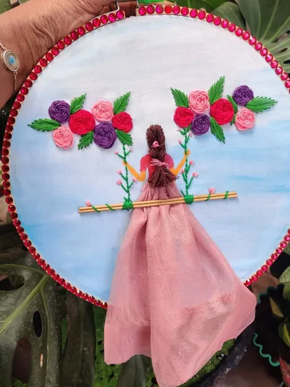 I create custom embroidery hoop art that tells a story. This piece features a girl on a swing, combining 3D fabric elements with delicate floral thread work, making for a whimsical and heartfelt piece of wall decor.