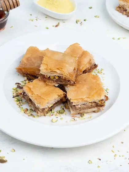 A plate of classic Baklava, a Turkish dessert. The bright, high-key lighting emphasizes the flaky layers of the pastry.