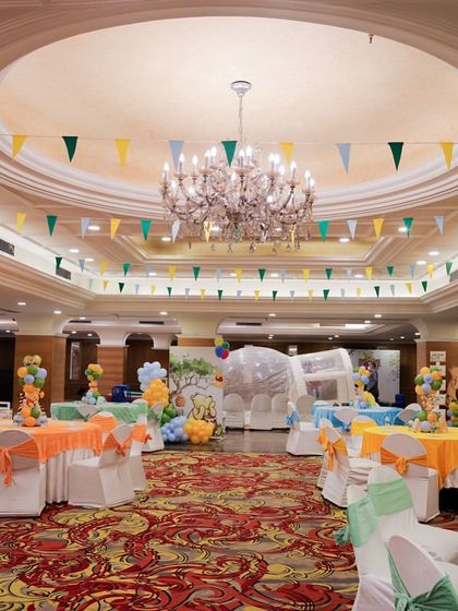 A wide view of the banquet hall decorated for the Winnie the Pooh theme. The tables are dressed in theme colors, and pennant banners hang from the ceiling, creating a festive atmosphere.