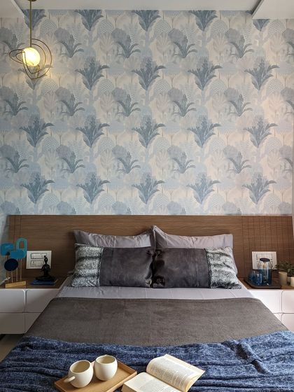 A cozy bedroom perfect for a rainy day. The blue patterned wallpaper and warm wooden headboard create a comforting atmosphere, ideal for relaxing with a book and a cup of coffee.