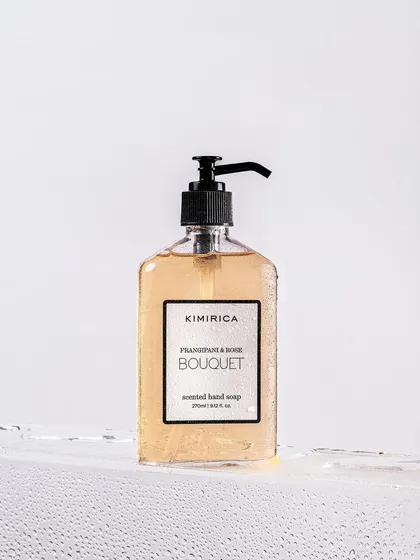 A clean, high-key shot of Kimirica's hand soap, focusing on the beautiful product design. The water ripple effect at the bottom adds a dynamic element and hints at the product's use.