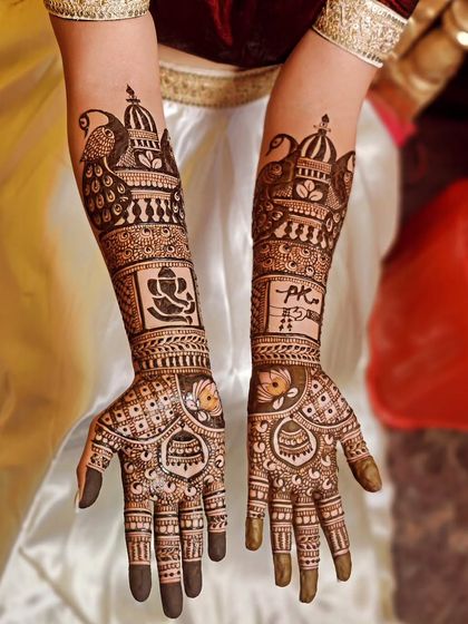 A personalized bridal mehendi featuring a Ganesha motif for blessings, the couple's initials, and traditional peacock and doli figures.