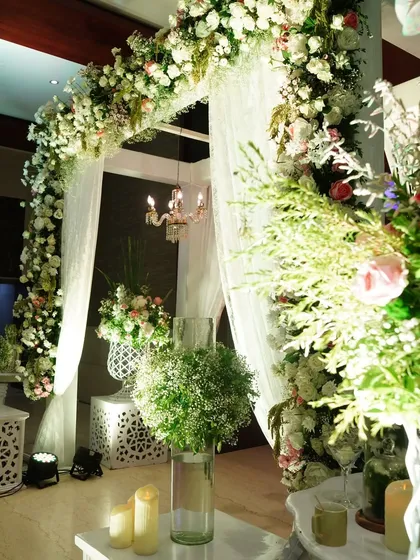 A close-up view of a beautiful white floral arch, accented with delicate baby's breath and soft lighting, perfect for a classic and elegant wedding theme.